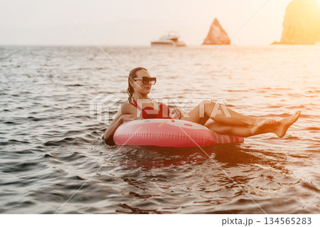 Woman, floating, water. Young woman relaxing on inflatable donut ring in calm sea at sunset with copy space. 134565283