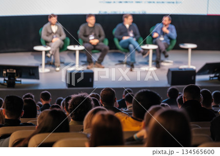 Panel discussion on stage with four speakers engaging audience in conference setting 134565600