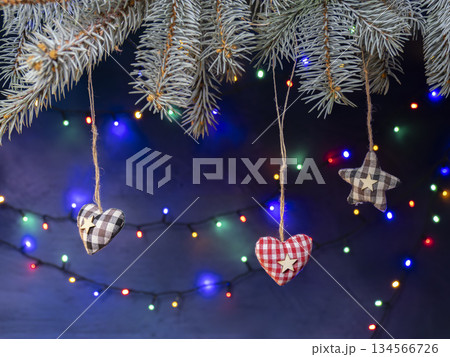 Hanging Fabric Hearts And Stars On Christmas Tree Branches With Colorful Holiday Lights Hanging Fabric Hearts And Stars On Christmas Tree Branches With Colorful Holiday Lights 134566726