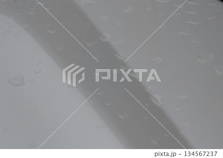 Close-up view of fresh rain water drops resting on smooth, clean white car surface after washing. 134567237