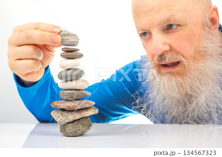 Enthusiastic older man smiling widely while engaged in building a stack of assorted stone Enthusiastic older man smiling widely while engaged in building a stack of assorted stone 134567323