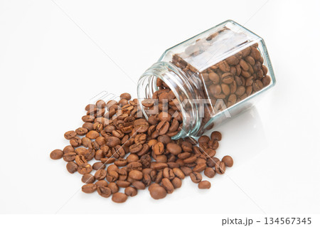 roasted coffee beans poured out of a glass transparent jar on a white background. 134567345
