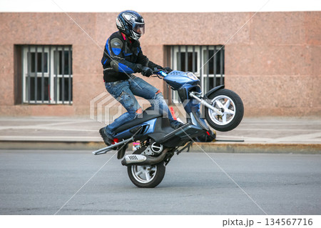 Biker balances on one wheel showcasing stunt skills on a city street Biker balances on one wheel showcasing stunt skills on a city street 134567716