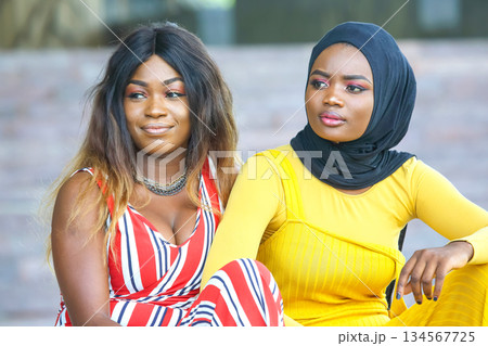 Two women enjoying a moment together in vibrant outfits outdoors during daytime Two women enjoying a moment together in vibrant outfits outdoors during daytime 134567725