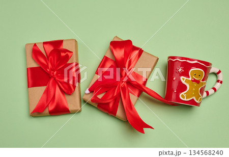 Gift box wrapped in craft paper and tied with a large bright red satin bow on a green background Gift box wrapped in craft paper and tied with a large bright red satin bow on a green background 134568240