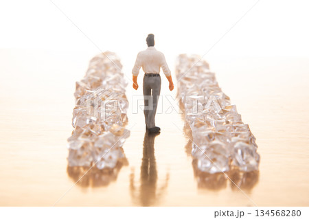 A small businessman walks between gleaming crystal piles on a reflective golden floor 134568280
