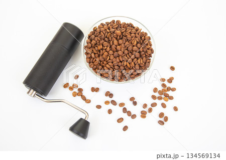 A sleek manual coffee grinder with a black textured body and metal handle stands beside a glass 134569134
