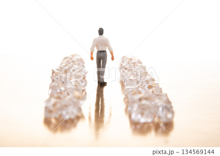 A small businessman walks between gleaming crystal piles on a reflective golden floor 134569144