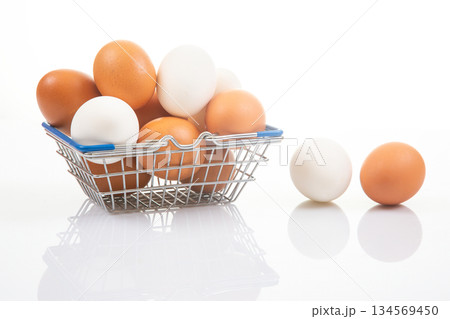 White and brown eggs in a wire shopping basket, accompanied by two eggs White and brown eggs in a wire shopping basket, accompanied by two eggs 134569450