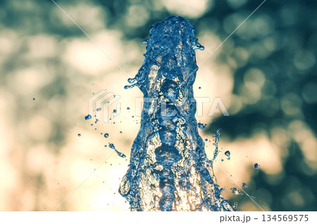 Water fountain sprays droplets against a blurred sunset background in a serene park setting 134569575
