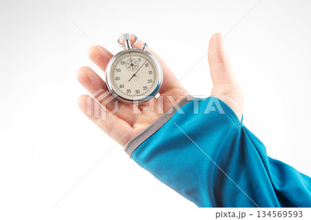 Hand holding silver stopwatch against a bright background in a sporty setting 134569593