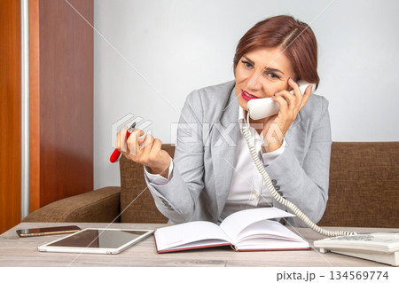 Businesswoman engaged in a phone conversation while working at a modern office desk Businesswoman engaged in a phone conversation while working at a modern office desk 134569774
