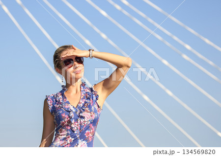 Woman shielding eyes from sun while standing under bridge on a bright day Woman shielding eyes from sun while standing under bridge on a bright day 134569820