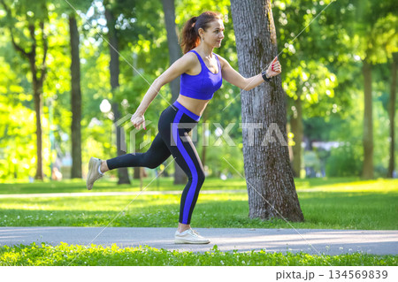 Young woman jogging in a sunny park surrounded by green trees and vibrant nature Young woman jogging in a sunny park surrounded by green trees and vibrant nature 134569839