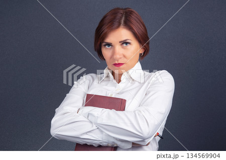 Confident businesswoman holding a book with arms crossed against a dark background 134569904