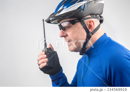 Cyclist communicates using a radio while wearing a helmet and sunglasses indoors Cyclist communicates using a radio while wearing a helmet and sunglasses indoors 134569919