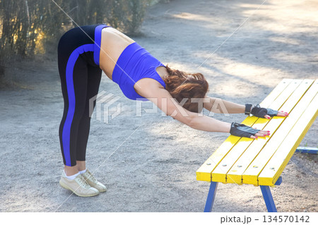 Woman performing stretching exercises outdoors at a park in bright daylight Woman performing stretching exercises outdoors at a park in bright daylight 134570142