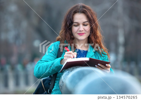 Woman writing in a notebook during a calm afternoon at a city park 134570265