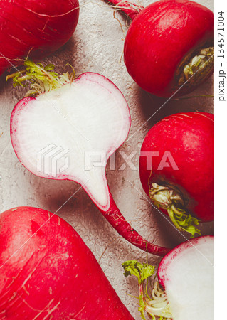 Fresh radishes on a light textured surface with one cut in half revealing white interior Fresh radishes on a light textured surface with one cut in half revealing white interior 134571004