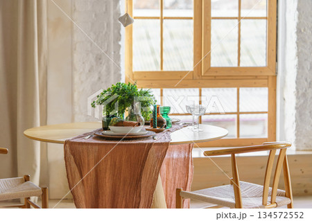 Cozy Scandinavian Christmas dining setting on table with natural decor on wide window background Cozy Scandinavian Christmas dining setting on table with natural decor on wide window background 134572552