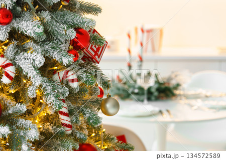 Frosted Christmas tree decorated with sparkling light and red ornaments on blurred dining background 134572589