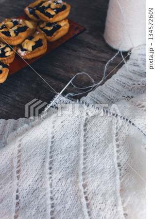 White knitting with beautiful pattern with cakes. Knitting needles and cotton knitting. Beautiful knitted pattern with cotton yarn ball and bakery tart. Knitting hobby. Knitwear concept. Cotton yarn White knitting with beautiful pattern with cakes. Knitting needles and cotton knitting. Beautiful knitted pattern with cotton yarn ball and bakery tart. Knitting hobby. Knitwear concept. Cotton yarn 134572609