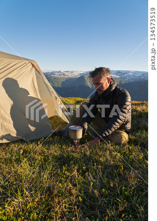 Hiker cooking on stove with shadow on tent in Norway mountains 134573519