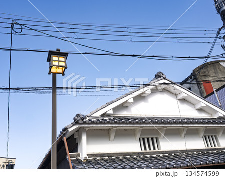 青空の下に佇むレトロな街灯と白壁の家屋 134574599