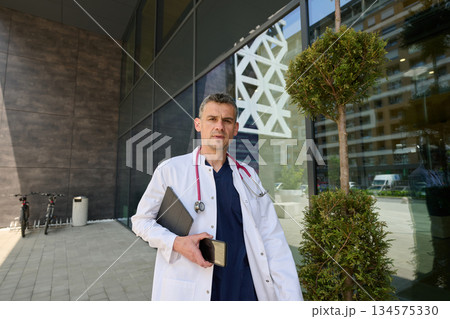 Doctor at a modern healthcare facility holding a tablet and phone while standing outside 134575330