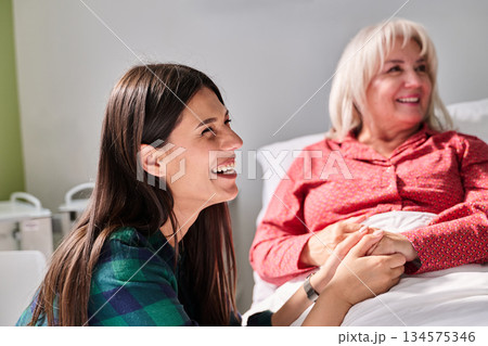Cheerful woman visiting elderly relative in a care facility, sharing smiles and warmth during a tender moment 134575346