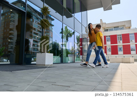 Woman and child walking together in urban setting near modern buildings during sunny day Woman and child walking together in urban setting near modern buildings during sunny day 134575361