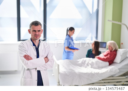 Doctor in a hospital room oversees nurses with patients during a routine check-up on a sunny morning 134575487