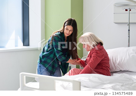 Caregiver assists elderly woman in hospital room during daytime visit for emotional support and companionship 134575489