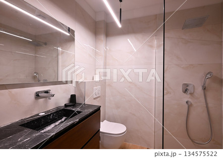 Luxurious modern bathroom featuring a sleek freestanding bathtub with a caddy, elegant vanity with sink and mirror, and a contemporary toilet. Soft tiled walls and wooden flooring create a spa-like 134575522
