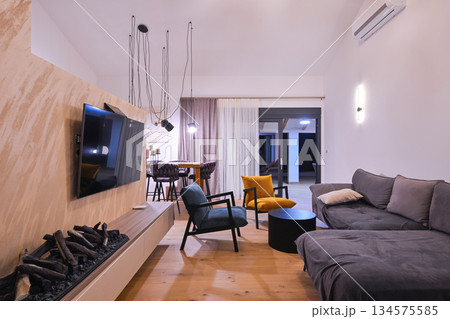 Modern open-plan living and dining area with an integrated kitchen, featuring a comfortable sofa, stylish armchairs, and a bar-height dining table. Wooden floors and ceiling beams enhance this Modern open-plan living and dining area with an integrated kitchen, featuring a comfortable sofa, stylish armchairs, and a bar-height dining table. Wooden floors and ceiling beams enhance this 134575585