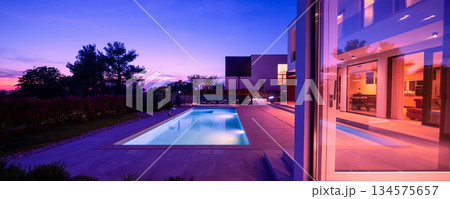 Modern luxury villa with a luminous swimming pool at twilight. Contemporary architecture, sleek design, and inviting interior lights create a serene and elegant evening ambiance, ideal for upscale Modern luxury villa with a luminous swimming pool at twilight. Contemporary architecture, sleek design, and inviting interior lights create a serene and elegant evening ambiance, ideal for upscale 134575657