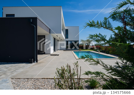 Modern luxury villa with swimming pool and clean minimalist architecture under a blue sky. Contemporary residential exterior featuring large windows, terrace, and elegant outdoor living space 134575666