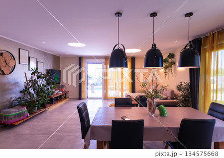 Bright modular house interior with modern open-plan living and dining room, large windows, indoor plants and cozy decor creating a warm, contemporary family home atmospher 134575668