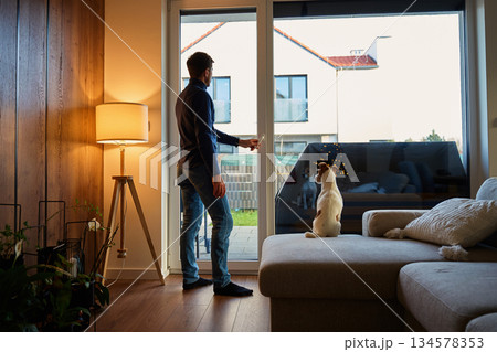 Man standing near large window with dog at home Man standing near large window with dog at home 134578353