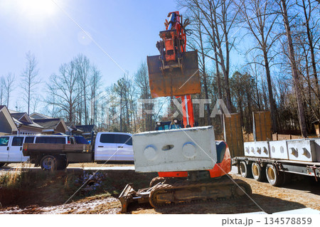 Heavy machinery lifts transports concrete blocks at construction site surrounded by vehicles. Heavy machinery lifts transports concrete blocks at construction site surrounded by vehicles. 134578859