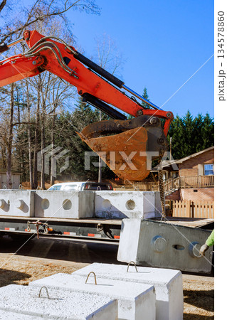 An excavator lifts concrete blocks to place them on construction site near house An excavator lifts concrete blocks to place them on construction site near house 134578860