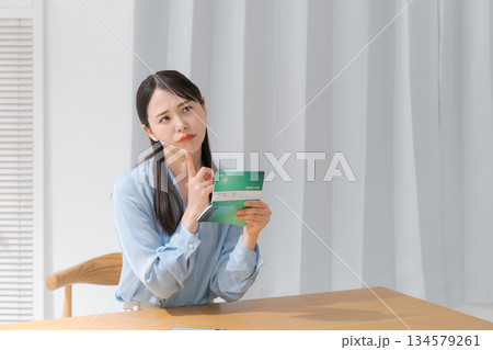 通帳を見て悩む女性 134579261