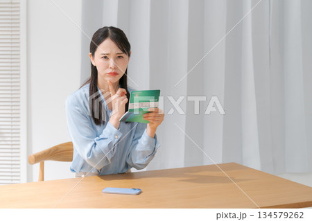 通帳を見て悩む女性 通帳を見て悩む女性 134579262