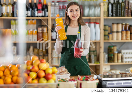 Experienced female salesperson offers choice of buying bottle of sweet carbonated water in grocery store 134579562
