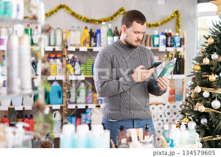 Middle-aged guy scanning QR-code on dishwashing liquid in store with New Year decoration Middle-aged guy scanning QR-code on dishwashing liquid in store with New Year decoration 134579605
