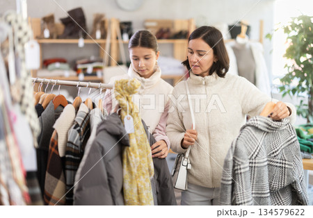 Mother and teen daughter looks at products in store and selects coat or jacket. Mother and teen daughter looks at products in store and selects coat or jacket. 134579622