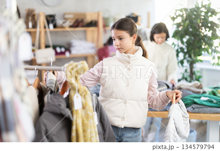 Teen girl looks at products in store and selects coat or jacket. Family shopping Teen girl looks at products in store and selects coat or jacket. Family shopping 134579794
