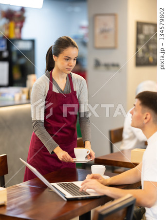 Female waitress brings coffee to guy working on laptop 134579802
