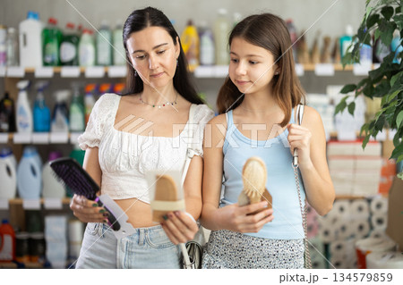 Preteen girl with mother choosing hair brushes in toiletries store 134579859