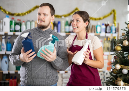 Professional young woman seller offers spray to male client in store. Christmas shopping Professional young woman seller offers spray to male client in store. Christmas shopping 134579876